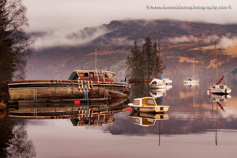 Misty morning reflections of Loch Ness in Scotland. Boats reflected as the morning mist dissipates near Fort Augustus.