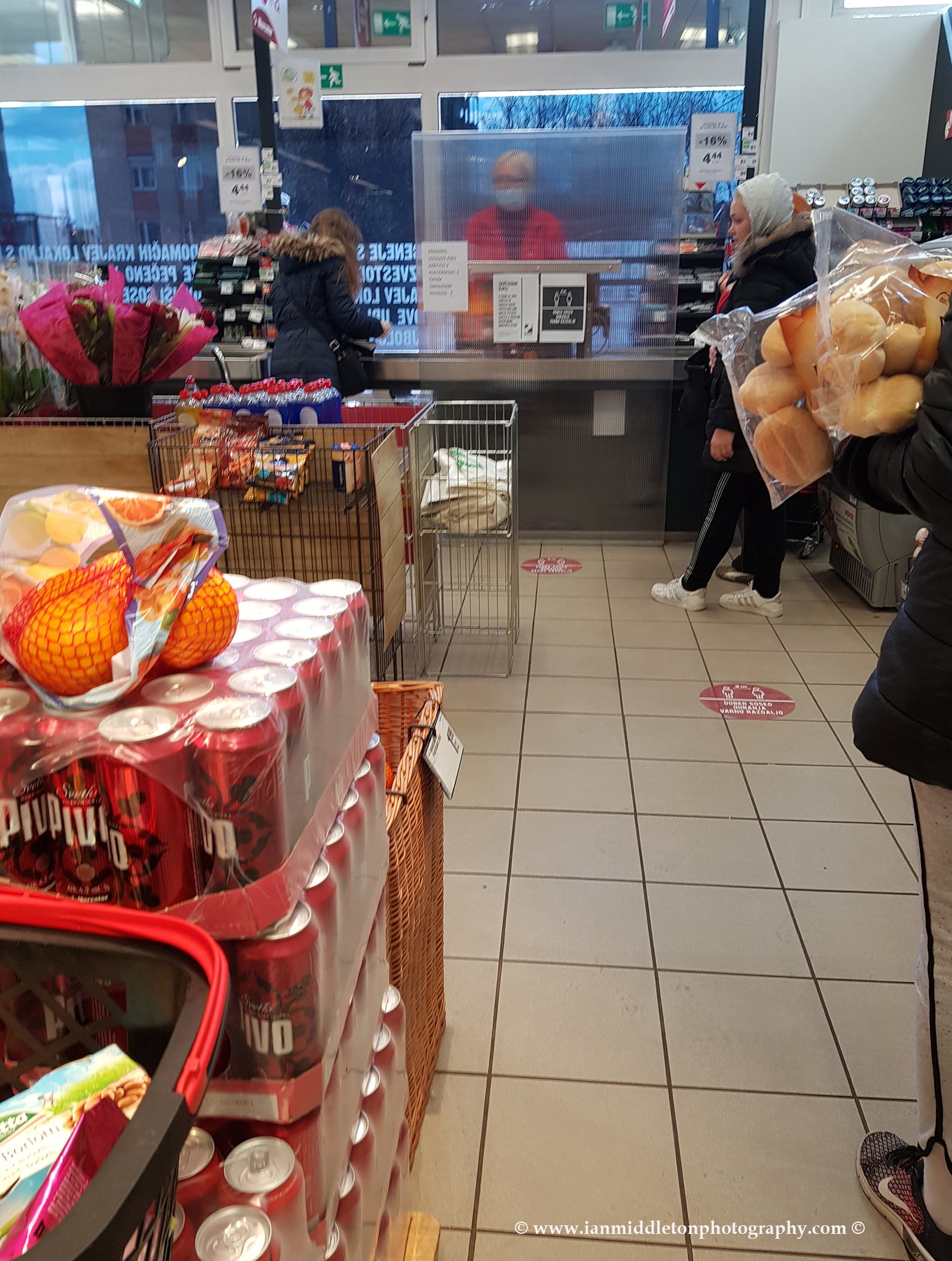 Queuing at the till in Mercator with the cashier behind a screen and wearing a mask. This is in a suburb of Ljubljana, Slovenia. Mercator is Slovenia's largest supermarket chain. Taken 23-3-2020