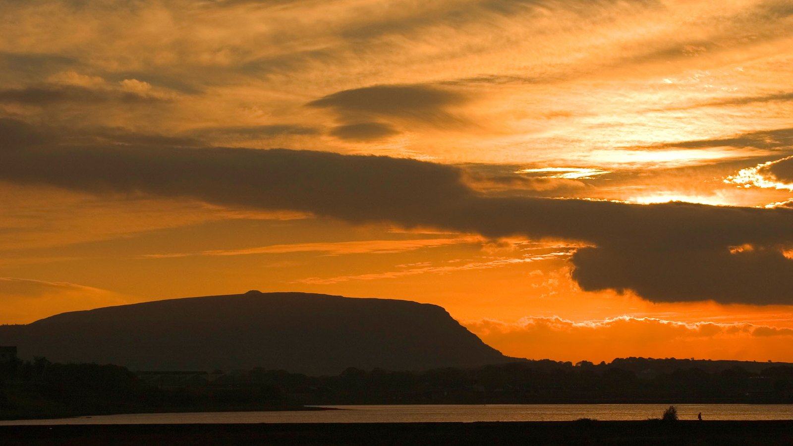 Sunset over Knocknarea Mountain and Sligo Bay, Ireland. The small mound on top of this mountain is the burial mound of Queen Maeve, the famous Queen who instigated the Táin Bó Cuailgne (Cattle Raid of Cooley). She is buried under a cairn of 40,000 tons of rock, which is 6000 years old. Legend says she is buried standing upright, spear in hand and facing Ulster, her enemy.